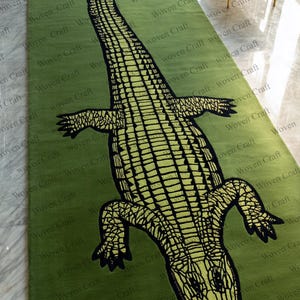May include: A green rectangular rug with a large, stylized alligator design in black and yellow. The words "Woven Craft" are printed repeatedly across the rug's surface.