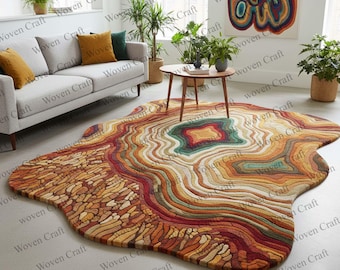 Puede incluir: Una alfombra grande, de forma irregular, con un diseño en capas en tonos marrones, naranjas, rojos y verdes. La alfombra tiene un patrón circular central y una apariencia texturizada, que se asemeja a una sección transversal de una geoda. La alfombra está colocada sobre un suelo claro.