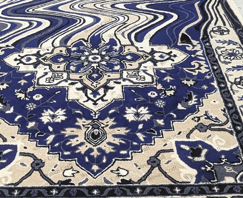 May include: A detailed close-up of a blue, beige, and cream-colored rug. The rug features a central medallion design with floral and geometric patterns. The border has a dark blue and cream design. The rug has a woven texture.