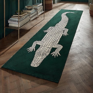 May include: A dark green rectangular rug with a large, off-white alligator design. The rug is placed on a wooden floor. The alligator design is a detailed, central feature of the rug.