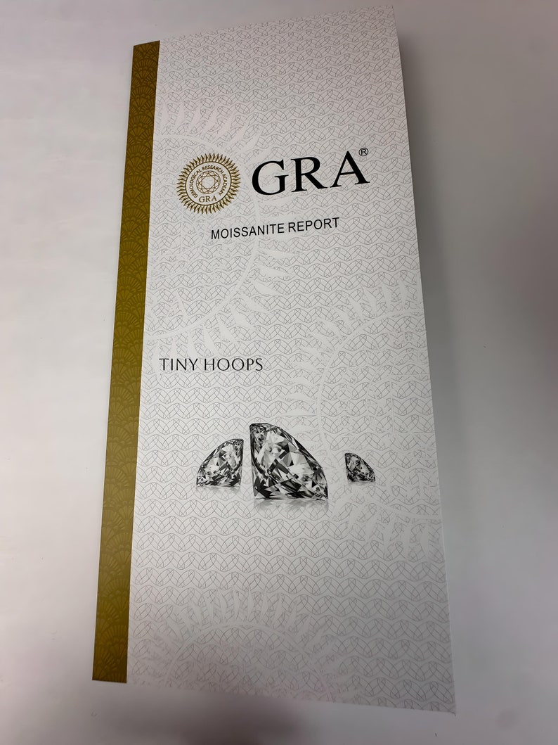 Op de afbeelding: Een wit en gouden moissanite-rapport met de tekst "GRA Moissanite Report" en "Tiny Hoops". Het rapport bevat een logo met de tekst "GRA" en een afbeelding van drie diamanten.
