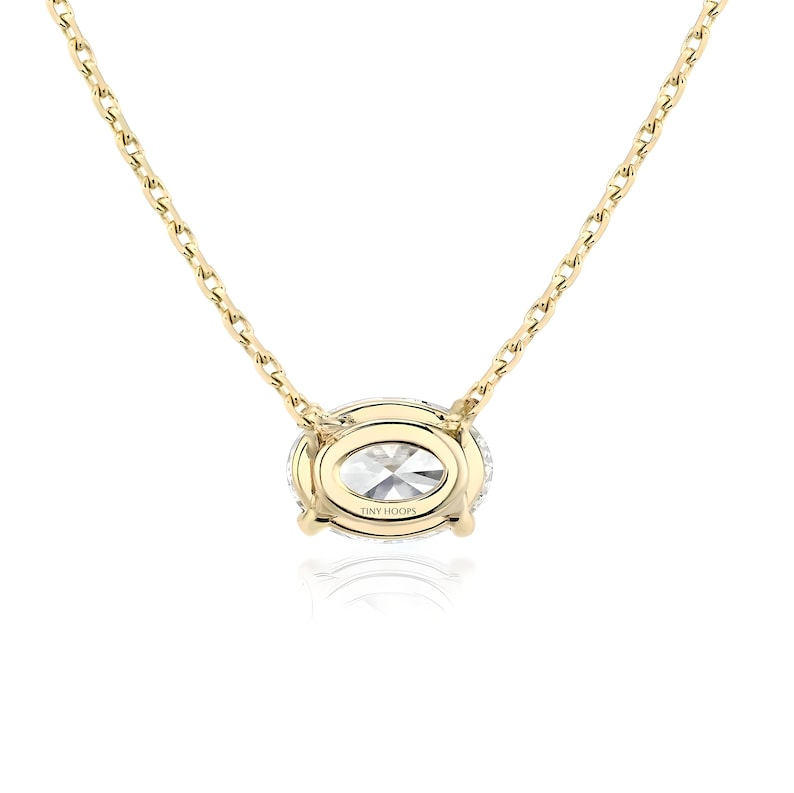May include: A gold chain necklace with a large oval-shaped pendant featuring a clear stone surrounded by smaller clear stones. The pendant is engraved with the text "TINY HOOPS".