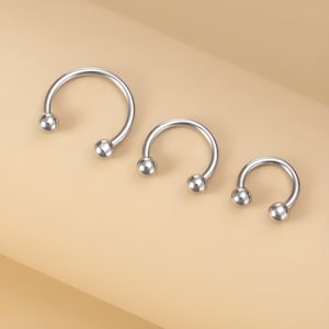 May include: Three silver horseshoe-shaped rings with ball ends. The rings are different sizes, with the largest ring on the left and the smallest ring on the right.