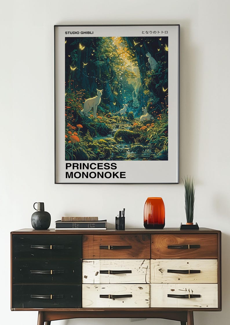 May include: A framed poster with a forest scene featuring a stream, trees, and white animals. The poster is titled "Princess Mononoke" and "Studio Ghibli" in black text. The Japanese text "もののけ姫" is also included.