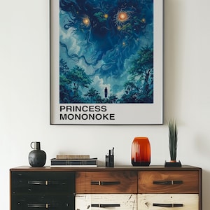May include: A framed poster of the Studio Ghibli film Princess Mononoke. The poster features a dark blue and green illustration of a forest spirit with glowing eyes. The text "Studio Ghibli" and "Princess Mononoke" is printed in black at the top and bottom of the poster. The poster is hanging on a white wall above a wooden dresser.