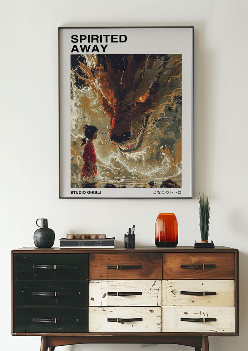 May include: A poster for the Studio Ghibli film "Spirited Away" featuring a young girl standing in front of a large, red dragon-like creature. The text "Spirited Away" and "Studio Ghibli" are visible at the top and bottom of the poster, respectively. The Japanese text "となりのトトロ" is also visible at the bottom of the poster.