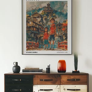 May include: A framed poster of the animated film "Spirited Away" by Studio Ghibli. The poster features the main characters Chihiro and Haku standing in front of a colorful, fantastical cityscape. The title "Spirited Away" and the Japanese title "となりのトトロ" are printed on the poster.