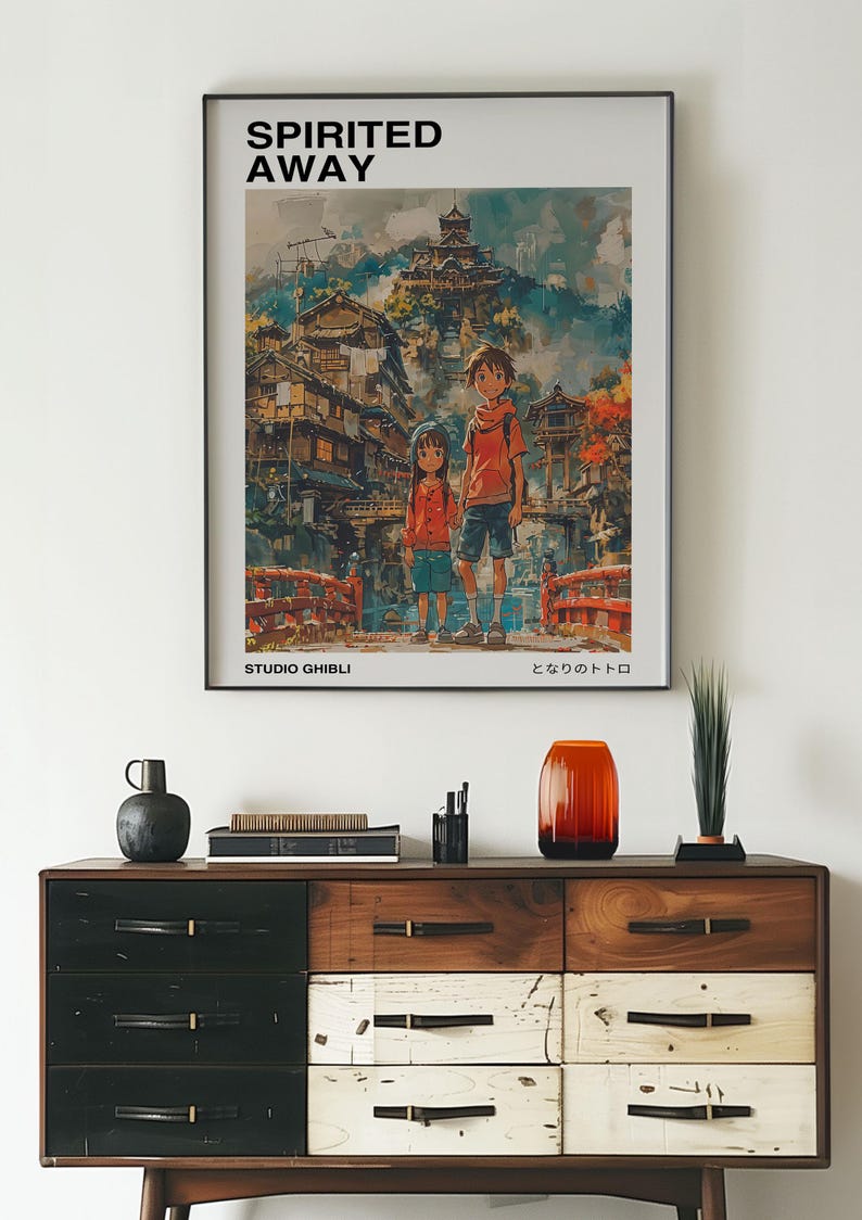 May include: A framed poster of the animated film "Spirited Away" by Studio Ghibli. The poster features the main characters Chihiro and Haku standing in front of a colorful, fantastical cityscape. The title "Spirited Away" and the Japanese title "となりのトトロ" are printed on the poster.