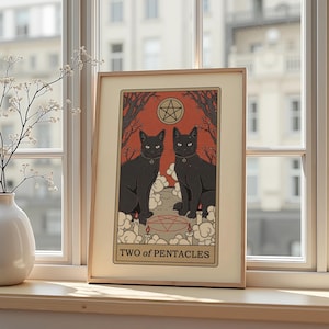 Può includere: Stampa artistica incorniciata con due gatti neri con collari, su sfondo rosso con un pentacolo e alberi. L'opera è intitolata "TWO of PENTACLES" in una cornice decorativa, che evoca un tema di tarocchi.