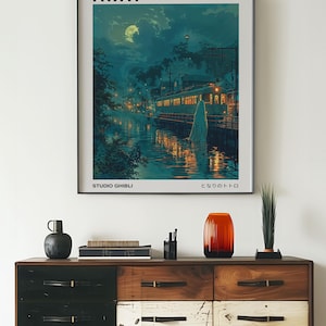 May include: A framed poster of the Studio Ghibli film "Spirited Away" with the Japanese title "となりのトトロ" and the text "Studio Ghibli" at the bottom. The poster features a nighttime scene with a train, a river, and a glowing figure.