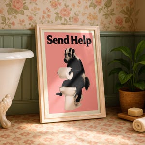 May include: Framed art print featuring a badger wearing a gas mask and sitting on a toilet, holding toilet paper. The text "Send Help" is displayed in bold black letters on a pink background. The frame is light beige.