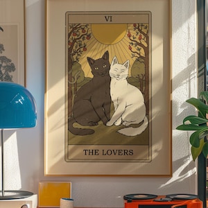 May include: A framed tarot card print featuring two cats, one black and one white, sitting together. The card is labeled "THE LOVERS" and has a warm, vintage aesthetic. The background includes trees, a sun, and the Roman numeral "VI".