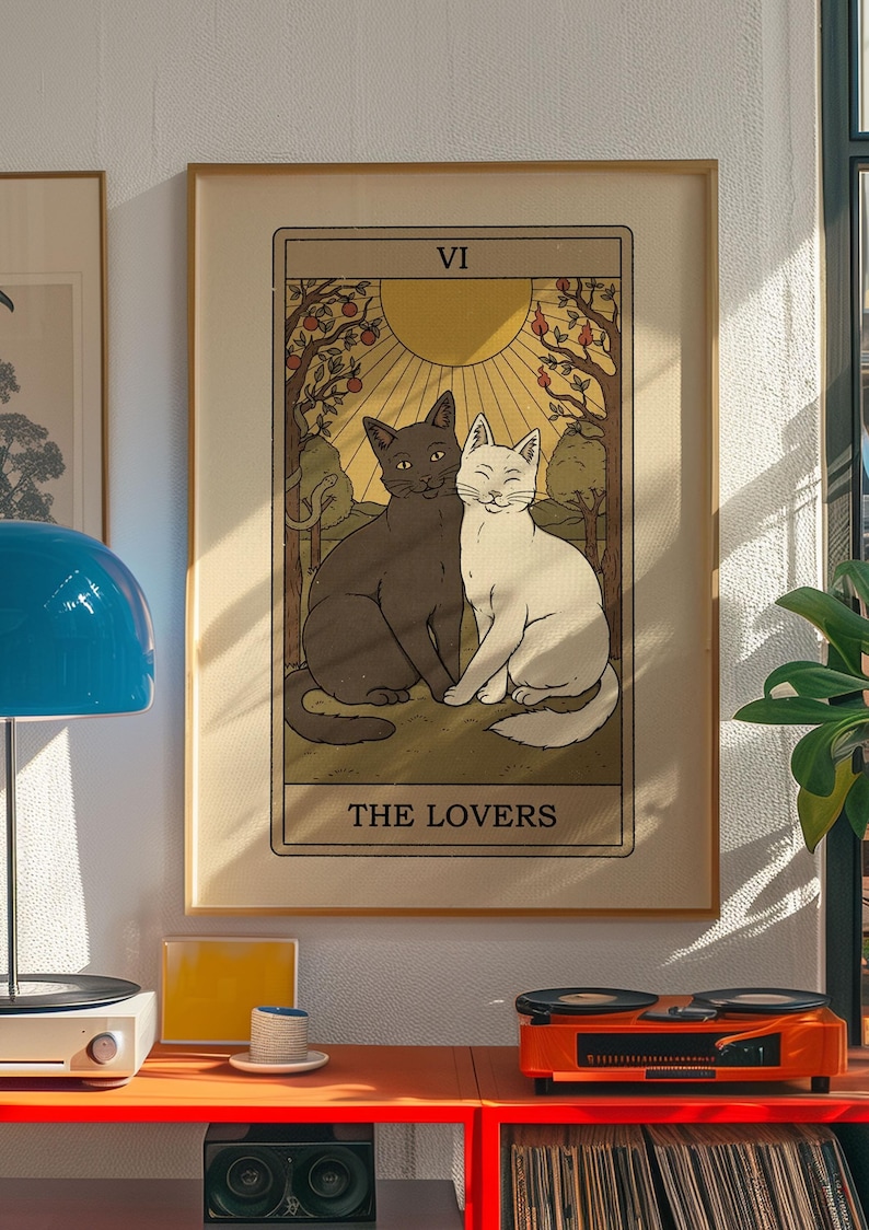 May include: A framed tarot card print featuring two cats, one black and one white, sitting together. The card is labeled "THE LOVERS" and has a warm, vintage aesthetic. The background includes trees, a sun, and the Roman numeral "VI".
