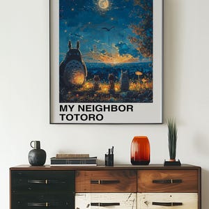 May include: A framed poster of the Studio Ghibli film "My Neighbor Totoro" featuring the titular character Totoro and two young girls sitting in front of a glowing moon and a cityscape in the distance. The poster is hanging on a white wall above a wooden dresser with drawers.