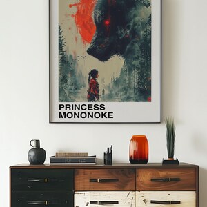 May include: A framed poster featuring a black and red illustration of a wolf and a young woman. The poster has the text "Studio Ghibli" and "Princess Mononoke" in black text. The poster is hanging on a white wall above a wooden dresser.
