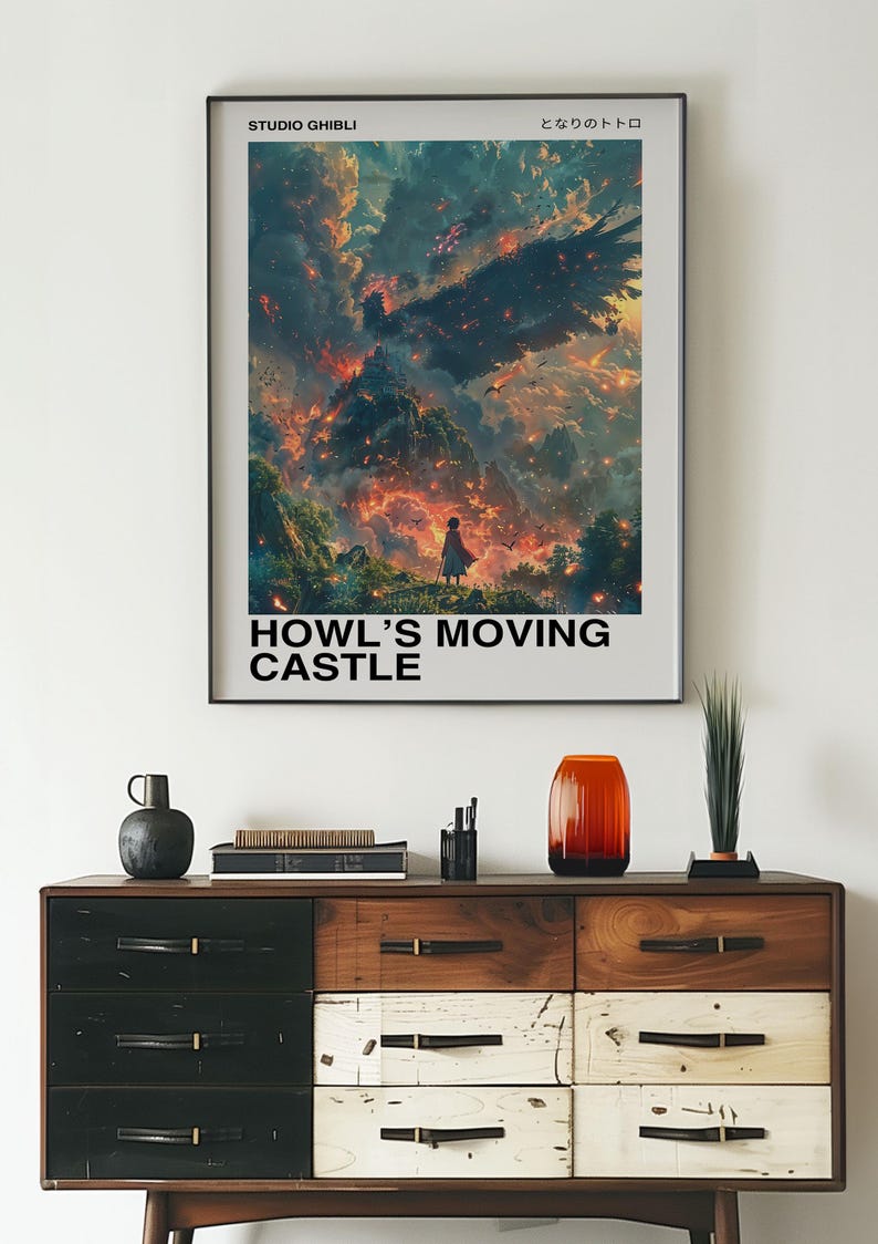May include: Framed poster featuring artwork from "Howl's Moving Castle." The image depicts a fiery landscape with a figure in the foreground. The poster has the text "HOWL'S MOVING CASTLE" and "STUDIO GHIBLI" at the top. The poster is displayed above a wooden dresser.