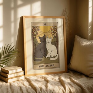May include: Framed art print featuring a tarot card design. The image depicts two cats, one black and one white, sitting together. The card reads "THE LOVERS" with the Roman numeral "VI" at the top. The artwork has a vintage aesthetic with a light brown frame.