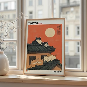 Può includere: Una stampa artistica incorniciata con un'illustrazione stilizzata di gatti su un tetto a Tokyo. L'opera d'arte ha una calda tavolozza di colori con un cielo arancione e una luna piena. Il testo include "TOKYO JAPAN" e "THE ROOF".