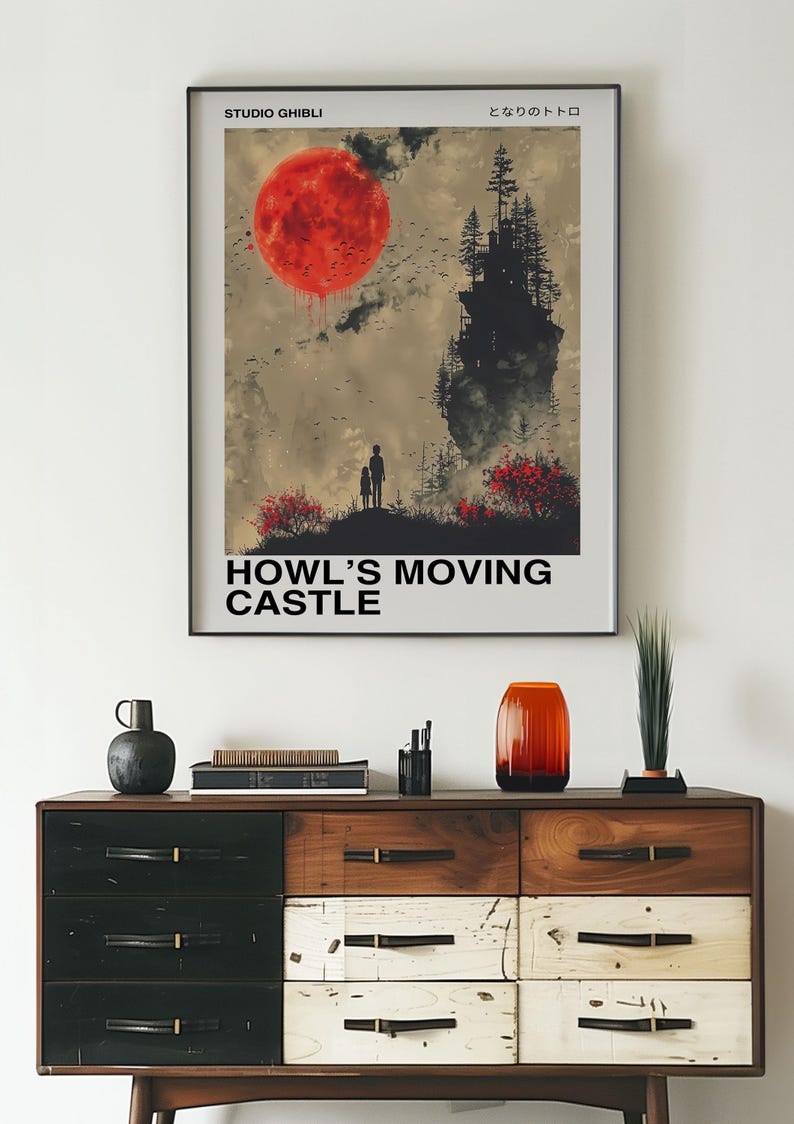 May include: Framed poster featuring a scene from "Howl's Moving Castle" with a large red sun, a silhouette of a castle, and the text "HOWL'S MOVING CASTLE". The poster is displayed above a wooden dresser with various decorative items.