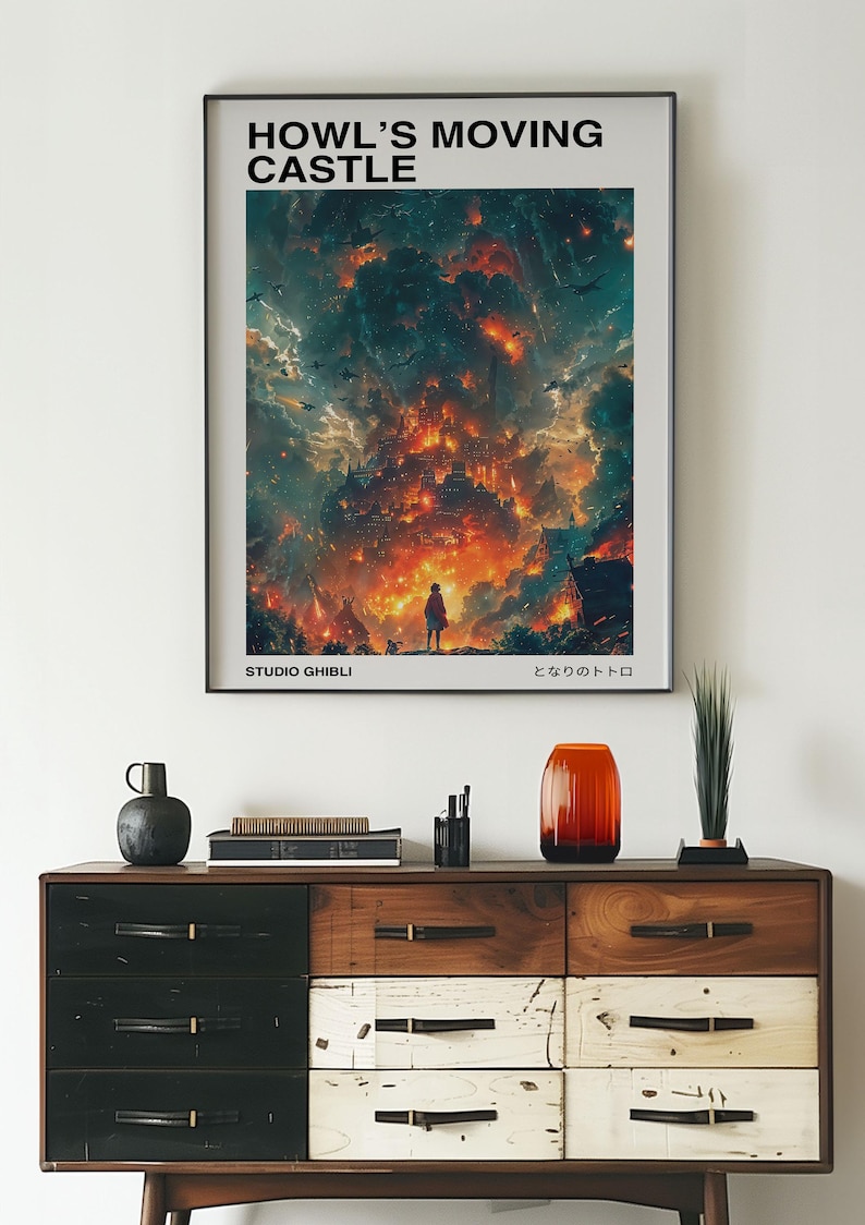 May include: A framed poster featuring the text "HOWL'S MOVING CASTLE" above a vibrant illustration of a fiery castle scene. The poster includes the text "STUDIO GHIBLI" and Japanese text. The poster is displayed above a wooden dresser.