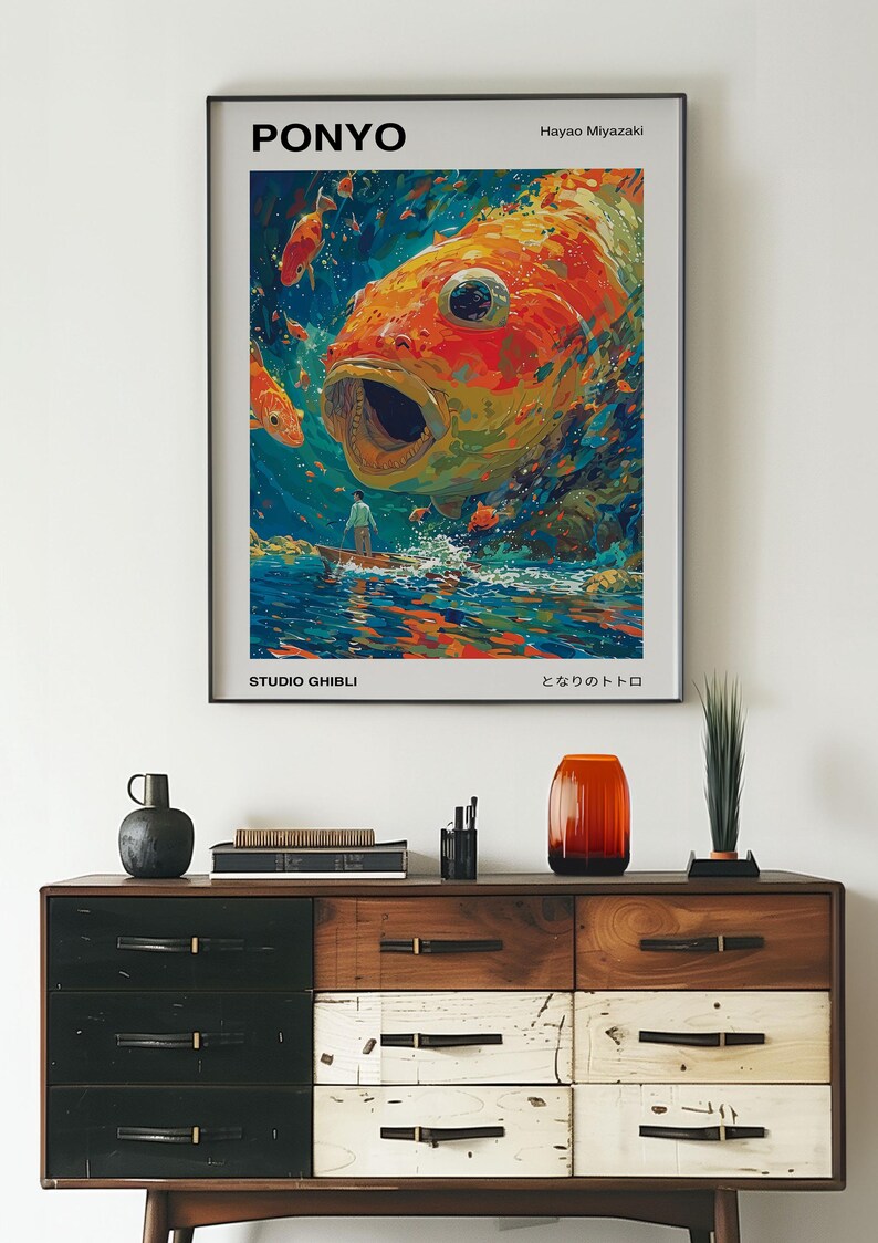 May include: A poster for the Studio Ghibli film "Ponyo" by Hayao Miyazaki. The poster features a large, orange and yellow fish with its mouth open, surrounded by smaller fish. The text "Ponyo" is in black letters at the top of the poster, and the text "Studio Ghibli" is in black letters at the bottom of the poster. The text "となりのトトロ" is in Japanese at the bottom of the poster.