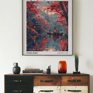 May include: A poster featuring a whimsical illustration of Totoro, a beloved character from the Studio Ghibli film "My Neighbor Totoro". The poster depicts Totoro sitting on a boat in a serene forest setting with a small house and a river in the background. The poster has the title "My Neighbor Totoro" and the text "Studio Ghibli" and "となりのトトロ" in Japanese.