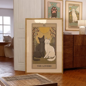 May include: Three framed tarot card art prints. The largest features a black and white cat illustration with the text "THE LOVERS" and "VI". The other two prints feature cat paw and cat illustrations. The frames are a light brown color.