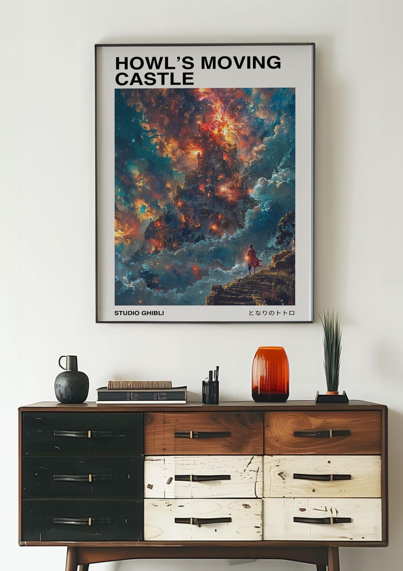 May include: Framed poster featuring the text "HOWL'S MOVING CASTLE" above a vibrant, colorful illustration of a fantastical landscape. The poster includes the text "STUDIO GHIBLI" and Japanese text. The poster is displayed above a wooden dresser.
