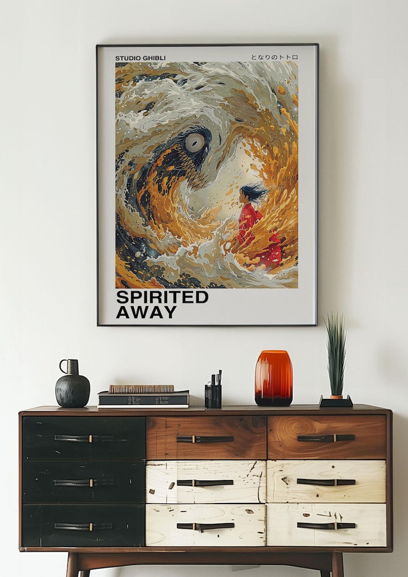 May include: A framed poster with a colorful illustration of a girl standing in front of a swirling wave. The poster is titled "Spirited Away" and features the text "Studio Ghibli" and "となりのトトロ" in Japanese.