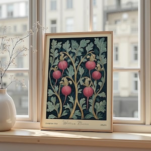 Può includere: Una stampa artistica incorniciata con un design botanico con frutta rosa e foglie verdi su sfondo blu scuro. La stampa è intitolata "William Morris" e "Exhibition 1983". La cornice è di colore legno chiaro.