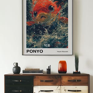 May include: A poster for the Studio Ghibli film "Ponyo" featuring a red fish with large eyes and a white background. The text on the poster reads "Studio Ghibli", "Ponyo", "Hayao Miyazaki", and "となりのトトロ" in Japanese.