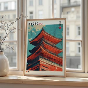 Può includere: Una stampa artistica incorniciata con un'illustrazione di una pagoda a Kyoto, in Giappone. L'opera presenta la pagoda in tonalità rosse e arancioni su uno sfondo celeste. La stampa include il testo "KYOTO JAPAN" e caratteri giapponesi.