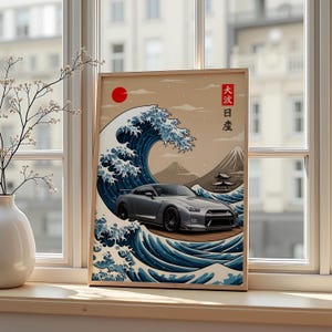 Könnte beinhalten: Gerahmter Druck mit einem silbernen Sportwagen vor dem Hintergrund eines japanischen Wellendesigns, einer roten Sonne und einem Berg. Das Kunstwerk enthält japanischen Text und wird auf einer Fensterbank ausgestellt.