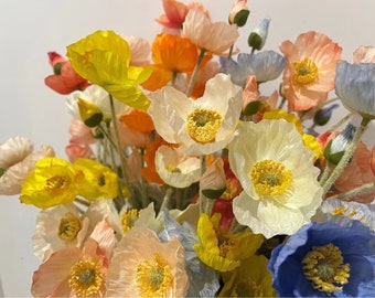 May include: A bouquet of silk poppy flowers in various colours, including yellow, white, pink, blue, and orange. The flowers are arranged in a vase and have a realistic appearance.