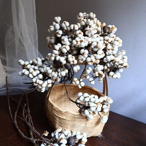 May include: A white dried flower arrangement in a woven basket. The flowers have small white berries and are arranged in a vase.