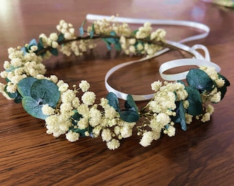 May include: A white flower crown with green leaves and a white satin ribbon.