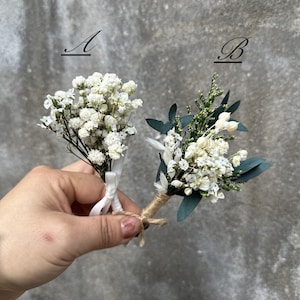 Könnte beinhalten: Zwei kleine Sträuße getrockneter weißer Blumen, einer mit weißem Band und der andere mit Schnur gebunden. Die Sträuße sind mit A und B beschriftet.