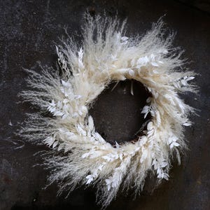Peut inclure: Une couronne de pampas et de feuilles blanches. La couronne est faite de pampas séchées et de feuilles blanches.