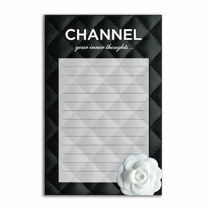 May include: A lined notepad with a white flower accent. The notepad has a black quilted border and a white interior with horizontal lines. The text "CHANNEL your inner thoughts..." is printed at the top.