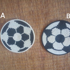 Pode incluir: Duas bases redondas tecidas, cada uma com um centro em espiral e segmentos alternados em preto e creme. As bases, rotuladas A e B, repousam sobre uma superfície texturizada castanho-clara.