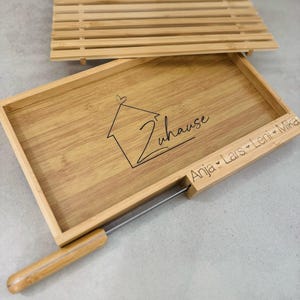Peut inclure: Un plateau de service en bois avec un porte-couteau. Le plateau est gravé des mots "Zuhause" et "Anja, Lars, Leni, Mika".