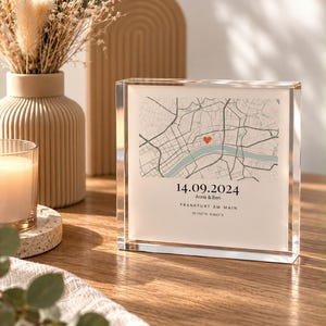 May include: A square acrylic block frame featuring a printed map of Frankfurt am Main with a red heart icon, the date 14.09.2024, the names Anna & Ben, and the coordinates 50.1102 N 8.6822 E printed in black text on a white background.