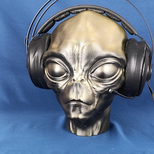 Könnte beinhalten: Eine graue Alien-Büste trägt schwarze Over-Ear-Kopfhörer mit einem Mikrofon.