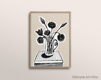 May include: A framed art print featuring a black and white illustration of flowers in a vase atop a stack of books. The artwork has a minimalist style with bold lines and a neutral background. The artist's name, Solaryne Art • Etsy, is in the bottom right corner.