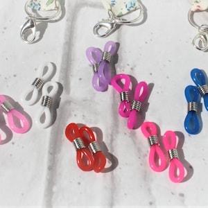 May include: Assortment of colourful plastic eyeglass chain connectors with silver metal clasps. The connectors are in various colours, including pink, blue, white, red, and black.