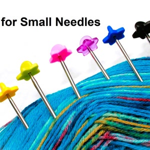 May include: Six colourful needle threaders with star-shaped tops, arranged on a ball of blue, green and yellow yarn. The threaders are made of metal with plastic tops. The text "for Small Needles" is visible at the top of the image.
