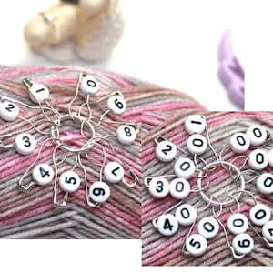 Op de afbeelding: Een set van tien witte plastic steekmarkeerders met zwarte nummers 0-9 op een bol roze en grijs garen.