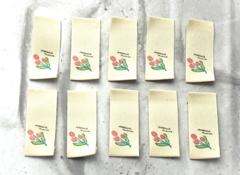 May include: Ten blank white fabric labels with a pink and green tulip design and the text "attach here" printed on each label.