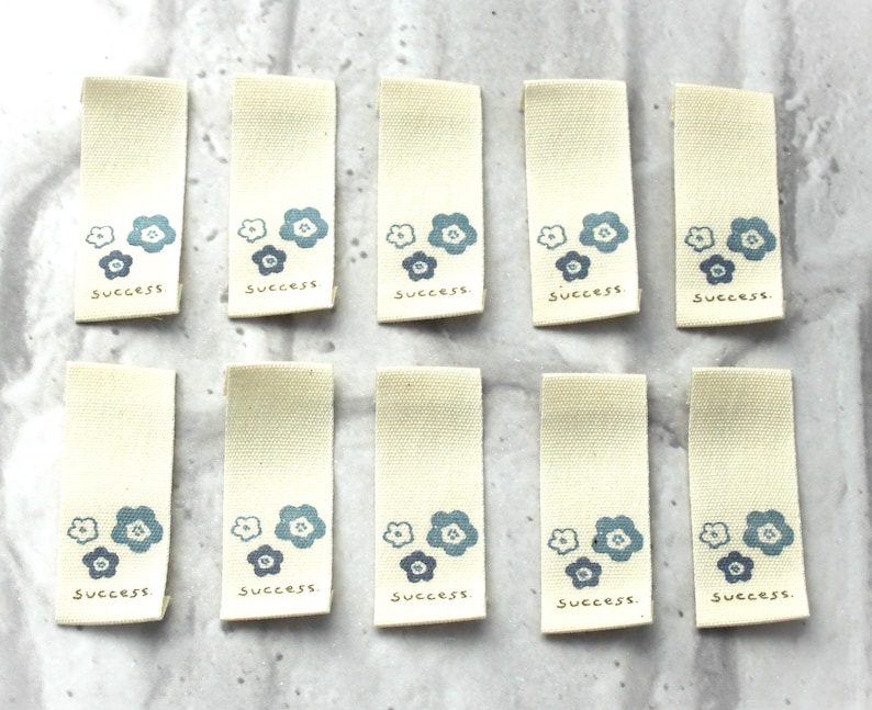 May include: Ten beige fabric tags with blue flower designs and the word "success" printed on each tag.