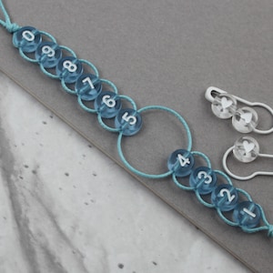 Può includere: Un anello di conteggio con perline blu e bianche con i numeri da 1 a 10. Sono inclusi anche due spilli di sicurezza con ciondoli a forma di cuore bianco.